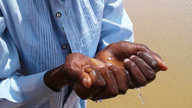 Miehen kädet täynnä vettä sadevedenkeruualtaan luona.