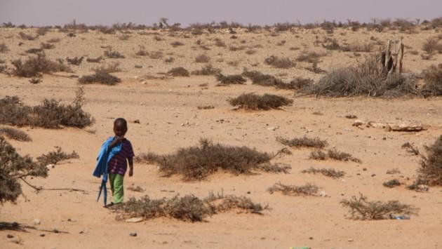 Lapsi kävelee keskellä aavikkomaisemaa.