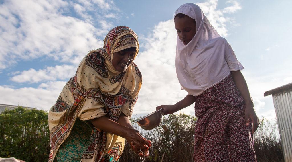 Äiti ja tytär pesemässä käsiä Somalimaassa kotitalon pihalla.