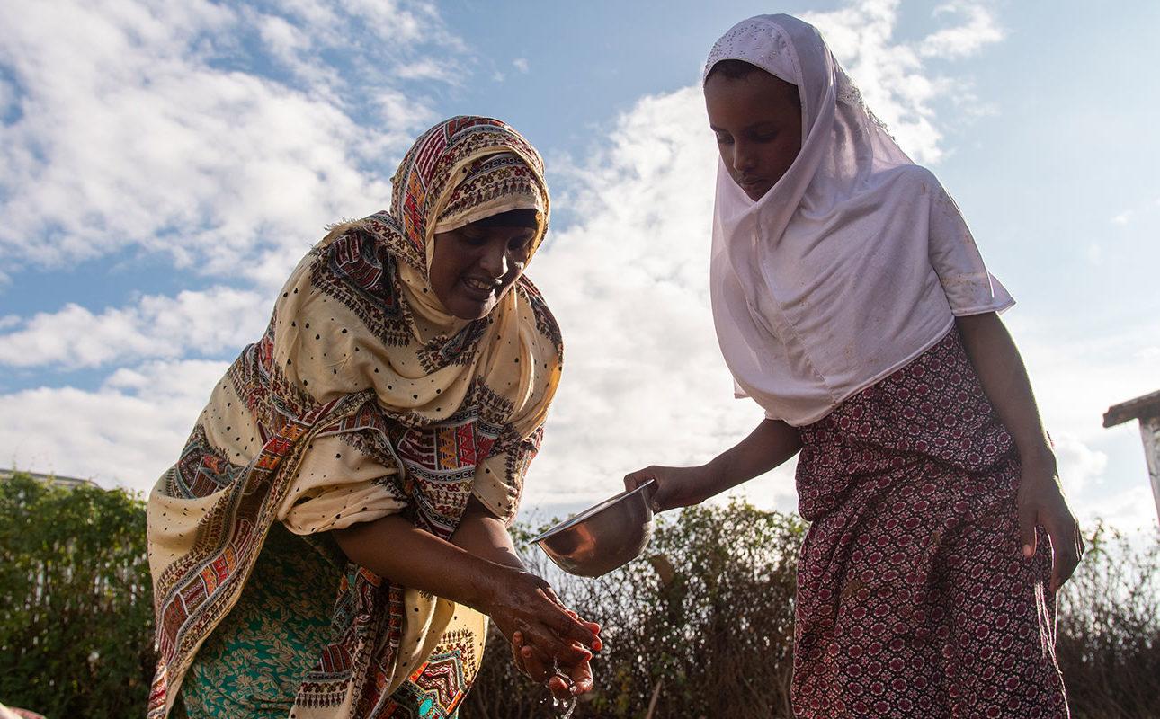 Äiti ja tytär pesemässä käsiä Somalimaassa kotitalon pihalla.