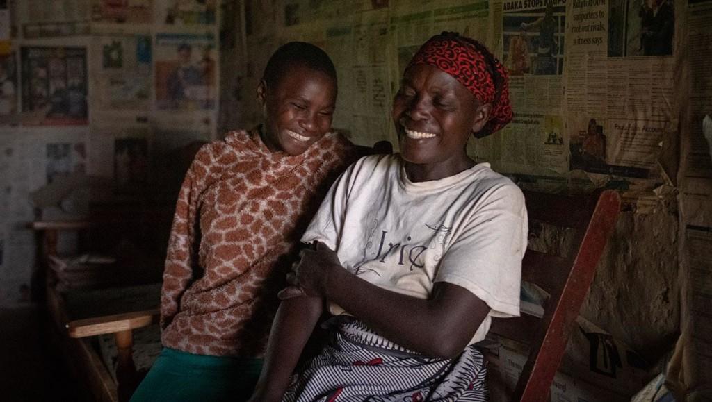 Kuvassa kenialainen äiti ja tytär istuvat lähekkäin ja nauravat.