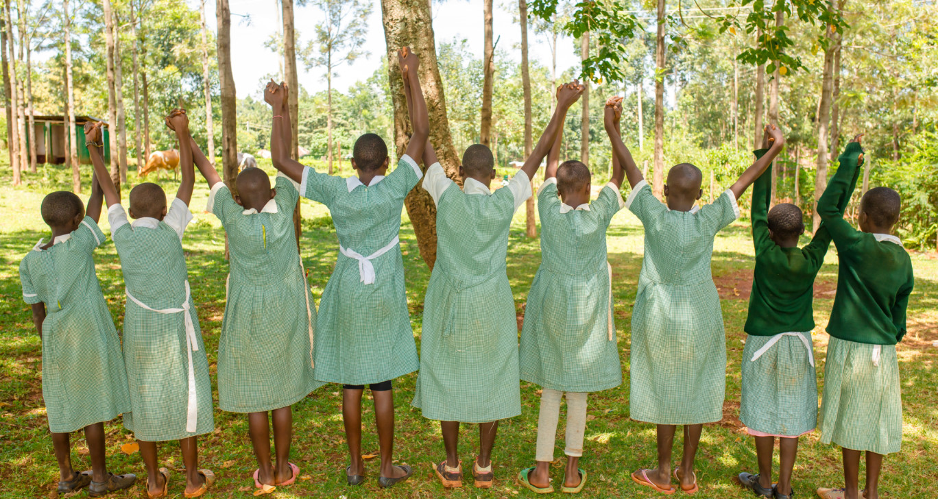 Yhdeksän kenialaistyttöä vihreä-valkoisissa kouluasuissa pitää toisiaan kädestä selin kameraan