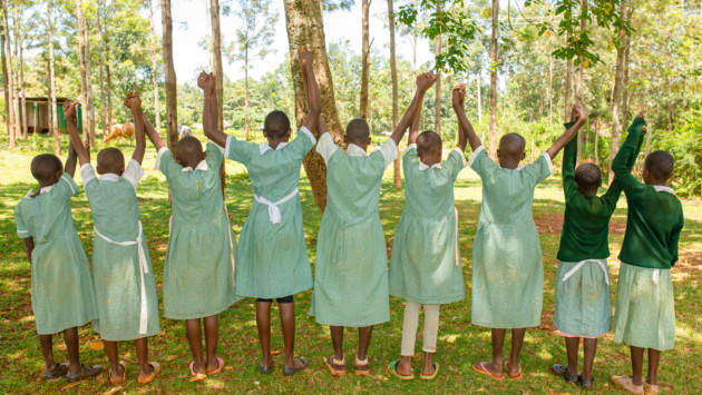 Yhdeksän kenialaistyttöä vihreä-valkoisissa kouluasuissa pitää toisiaan kädestä selin kameraan
