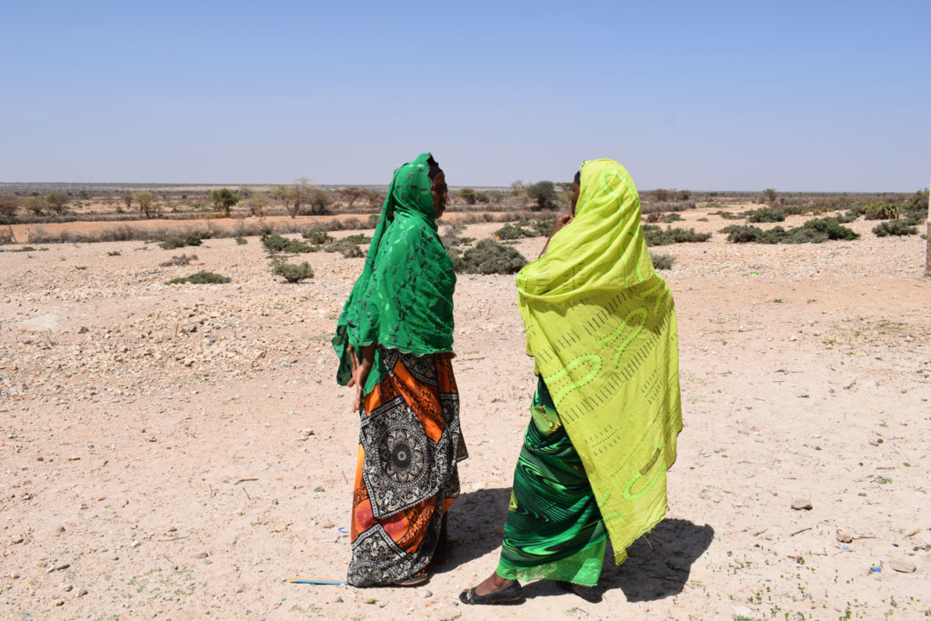 Kaksi huiveihin pukeutunutta naista seisoo keskellä aavikkonäkymää.